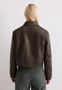 Braune Leder-Cropped-Jacke mit einem Reverskragen und minimalen Nähten. Glatte Textur, einfaches Design und strukturierte Passform.