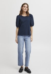 T-shirt bleu marine à manches bouffantes avec des broderies florales, associé à un jean droit bleu clair et des mocassins noirs.