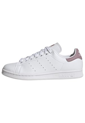 Biały sneaker Adidas Stan Smith z perforowanymi trzema paskami, białymi sznurowadłami i fioletowym elementem na pięcie na białym tle.
