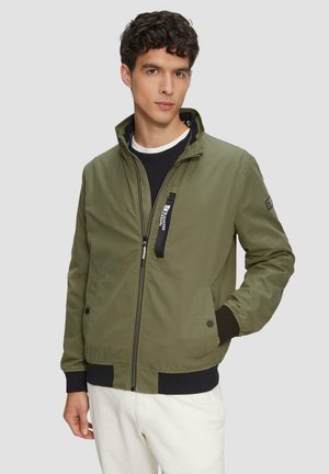 Olive green bomber jacket featuring a stand-up collar, front zip closure, and contrasting black cuffs. Includes side pockets and branding detail.