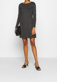 Ljusgrå långärmad klänning med en något utsvängd fåll, kombinerad med svarta klacksandaler med remmar och en strukturerad svart handväska.