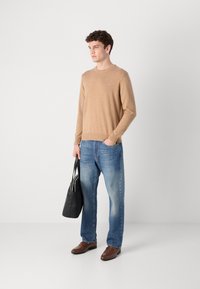 Bézs kötött pulóver kerek nyakkal, világoskék farmernadrággal párosítva. Fekete bevásárlótáskát tart. Barna slip-on cipők egészítik ki az öltözetet.