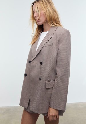 Blazer croisé en motif pied-de-poule, avec des boutons foncés, un col cranté et des épaules structurées, confectionné dans un tissu texturé.