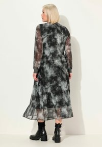 Długa czarna i szara sukienka tie-dye z przezroczystymi długimi rękawami, teksturowanym górą i zwiewnym dołem, w połączeniu z czarnymi platformami.