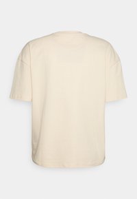 Cremefarbenes T-Shirt mit kurzen Ärmeln und lässigem Schnitt. Weiches Baumwollmaterial, runder Ausschnitt und fallende Schulternähte.