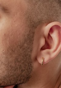 Orecchino a cerchio d'oro attaccato a un orecchio rasato, con una finitura liscia e lucida e una leggera curvatura nel design.