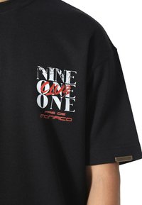 Sort bomulds t-shirt med fed hvid og rød grafisk tekst, med "NINE CLUB ONE" og "PAS DE MONACO" på fronten, kortærmet.
