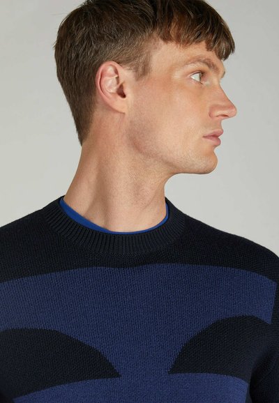 Knit sweater featuring navy and dark blue stripes, round neckline, and textured fabric. The design includes abstract patterns on the chest.