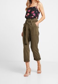 Svart blommig linne med rosa och blå blommor. Olivgröna högmidjade cargobyxor med knytbälte. Beiga remsandaler med klack.