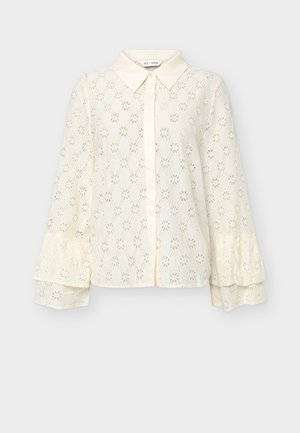 Kremowa koronkowa bluzka z długimi, warstwowymi rękawami w kształcie dzwonu, ostrym kołnierzykiem i zapięciem na guziki z przodu.