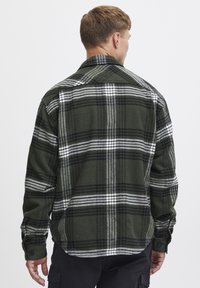 Cămașă din flanel ecologic, cu carouri verzi și alb-negru, mâneci lungi și manșete cu nasturi. Textură moale, guler clasic și margine dreaptă.