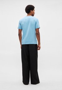 Világoskék, rövid ujjú, kerek nyakú póló, fekete, bő szárú nadrággal párosítva. Sima textúra, laza szabás.