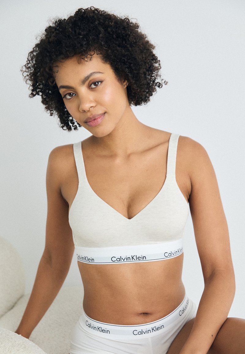 Ανοιχτό γκρίζο bralette με σχέδιο V στο λαιμό, φαρδιές τιράντες και ελαστική ζώνη με το λογότυπο Calvin Klein. Μαλακό ύφασμα με λεία υφή.