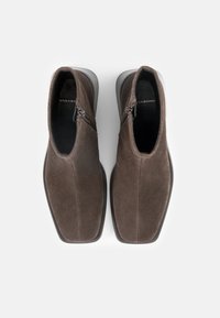 Stivaletti alla caviglia in suede marrone con una texture liscia, chiusura con zip sul lato e design della punta arrotondata. Suola in gomma a contrasto per una maggiore aderenza.