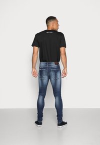 Camiseta preta com o texto "NIGHT ADDICT", combinada com jeans skinny azuis elásticos com detalhes desgastados e dois bolsos nas costas. Sapatos pretos.