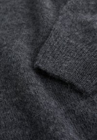 Mörkgrått stickat tyg med en mjuk, fluffig textur. Närbild visar ribbad detaljering och nyansvariationer genom hela materialet.