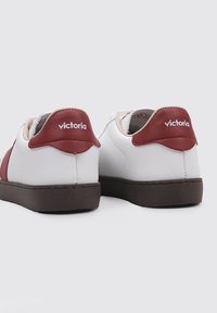 Sneaker bianche con esterno in pelle liscia, suole in gomma marrone e dettagli bordeaux sul tallone con il marchio "victoria".