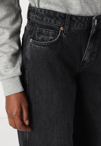 Black denim jeans with a high waist, featuring a classic five-pocket design, copper rivets, and subtle fading on the fabric.