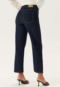 Mörkblå denimjeans med rak passform, med gula sömmar, två bakfickor och en läderpatch på midjan.