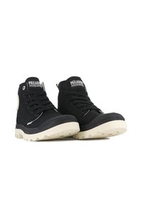 Zapatillas altas negras con parte superior de lona, suela de goma crema en contraste, cordones prominentes y detalle del logo en la lengüeta.