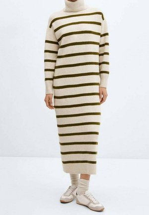 Robe en tricot beige longue avec des rayures verticales vert foncé, col haut et manches longues. Associée à des baskets claires et des chaussettes.