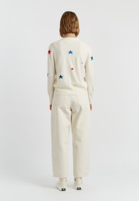 Maglione color crema con ricami di stelle colorate, abbinato a pantaloni leggeri color crema. Vestibilità casual, polsini e orlo a coste.