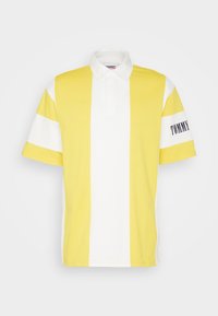 Yellow and white striped polo shirt featuring a collar, short sleeves, and "TOMMY" logo on the sleeve. Cotton fabric with a smooth texture.