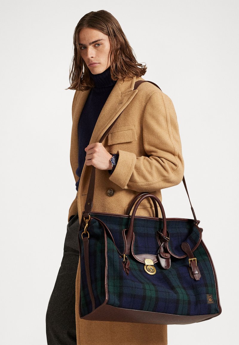 Plaid tote bag in navy and green, with brown leather accents, two handles, and detachable strap. Features a brass lock and buckle detail.