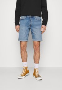 Vaaleansiniset farkkushortsit klassisella leikkauksella ja käännetyillä hupenevilla lahkeilla, yhdistettynä vaaleanruskeisiin korkeakorkoisiin tennareihin ja valkoisiin sukkiin.