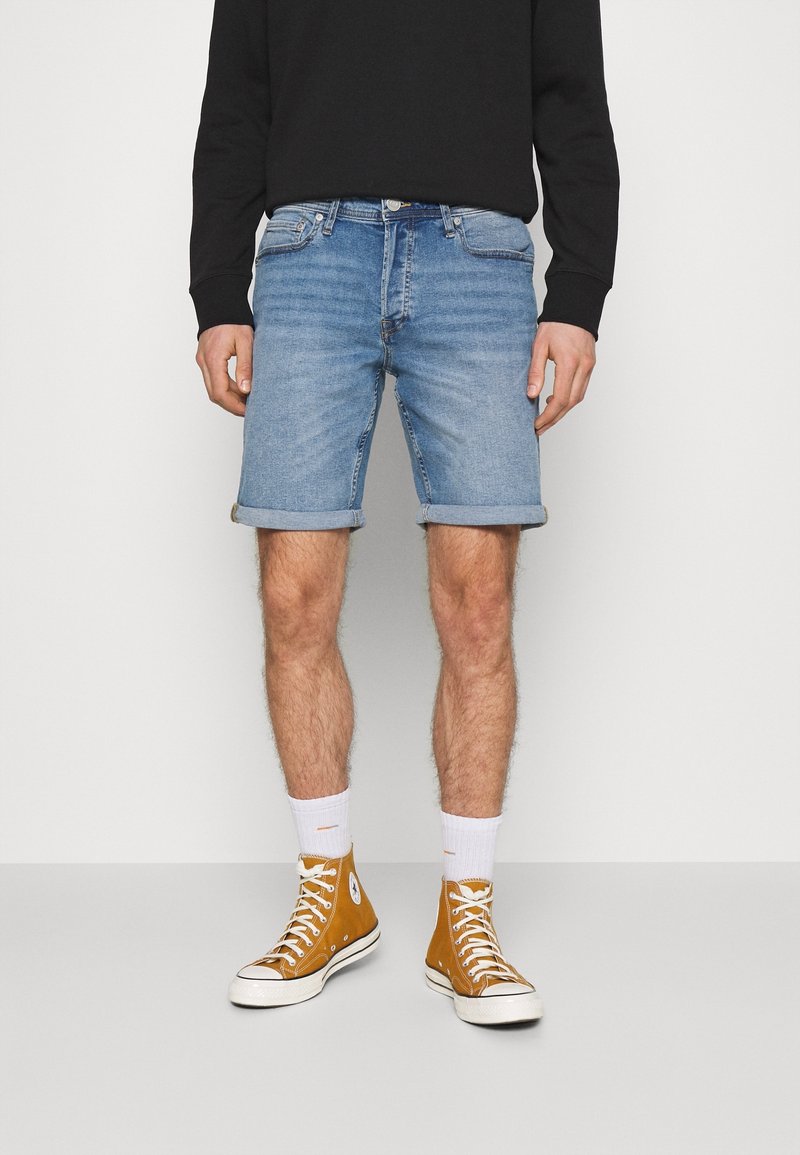 Vaaleansiniset farkkushortsit klassisella leikkauksella ja käännetyillä hupenevilla lahkeilla, yhdistettynä vaaleanruskeisiin korkeakorkoisiin tennareihin ja valkoisiin sukkiin.