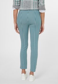 Turkooise en witte gemusterde leggings met een aansluitend design, voorzien van een visgraatpatroon en gecombineerd met witte sneakers.