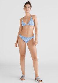 Conjunto de biquíni em azul claro com riscas brancas de zebra, parte superior triangular com alças finas e parte de baixo de cintura baixa a condizer, combinado com sandálias azuis.