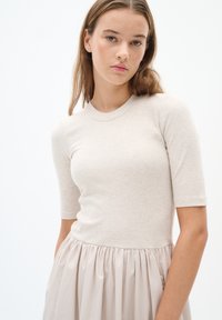 Beige gerippter Strickoberteil mit kurzen Ärmeln, kombiniert mit einem weichen, plissierten Chiffonrock in einem helleren Beigeton. Glatte Textur, taillierter Sitz.