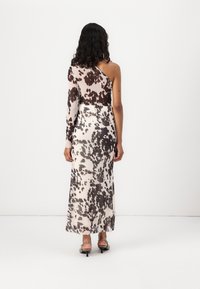 Robe asymétrique avec un imprimé vache marron et crème, en tissu léger. Elle présente une silhouette fluide et une fente à l'ourlet.