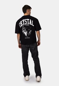 Černé tričko s velkým grafikou vlka a nápisem "CRYSTAL Paris" v bílé barvě. Nosené s tmavými džíny a bílými teniskami.