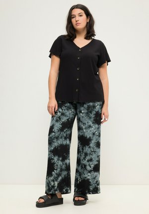 Top nero a costine con maniche a sbuffo corte e chiusura con bottoni, abbinato a pantaloni larghi con un motivo tie-dye blu e nero. Sandali platform neri.