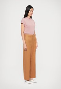 Un haut rose clair à manches courtes associé à un pantalon camel à taille haute et jambes larges, le tout accompagné de talons aiguilles blancs, créant une silhouette moderne et épurée.
