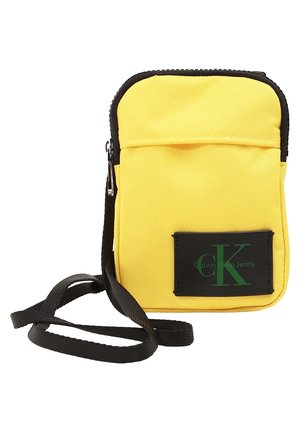 Bolso bandolera amarillo de Calvin Klein Jeans con cremallera negra, parche con logo negro y correa negra ajustable.