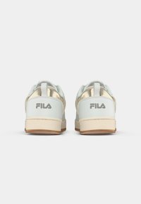 Hvite og lysegrønne sneakers med metallisk gullakenter og beige gummisåler. Fila-logoen vist på baksiden. Glatt lær og mesh-materialer.