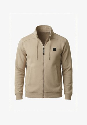 Chaqueta beige con cremallera, cuello alto, bolsillos delanteros, cordones ajustables, puños acanalados y un pequeño logo cuadrado negro en el pecho izquierdo.