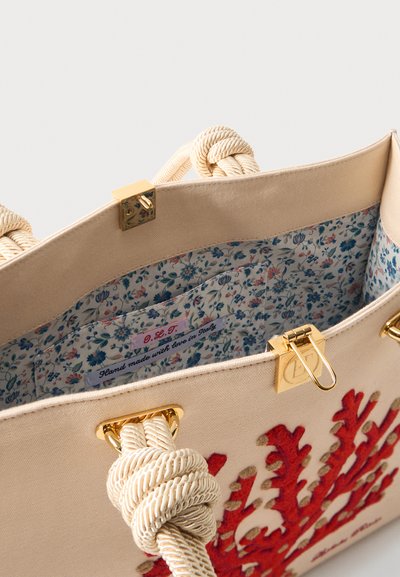 Μπεζ τσάντα tote με χοντρές, δεμένες λαβές από σχοινί, κόκκινη κεντημένη κοράλλι, χρυσούς κλιπ, και λουλουδάτο εσωτερικό επένδυση με ετικέτα «Χειροποίητο με αγάπη στην Ιταλία.»