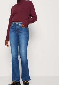 Bordeaux-randig tröja i ribbad kvalitet som kombineras med högmidjade blå utsvängda jeans. Jeansen har en klassisk femficksdesign och en lätt tvättning. Svarta skor med gulddetaljer.