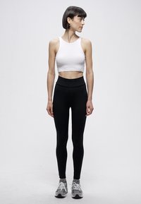 Hvit kort sommertrøye og svart leggings med høy midje. Modellen har på grå treningssko. Enkel, tettsittende design uten synlige mønstre.