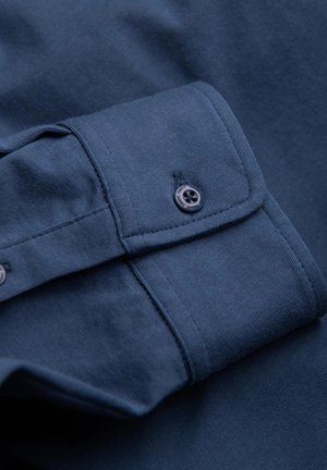 Mörkblå bomullsskjorta med detalj av slät textur och knappmanchetter. Har en enkel svart knapp och förstärkta sömmar.