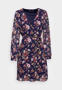 Vestido envolvente floral em azul marinho, com mangas longas transparentes, decote em V e cintura atada. O tecido apresenta um padrão colorido de flores.