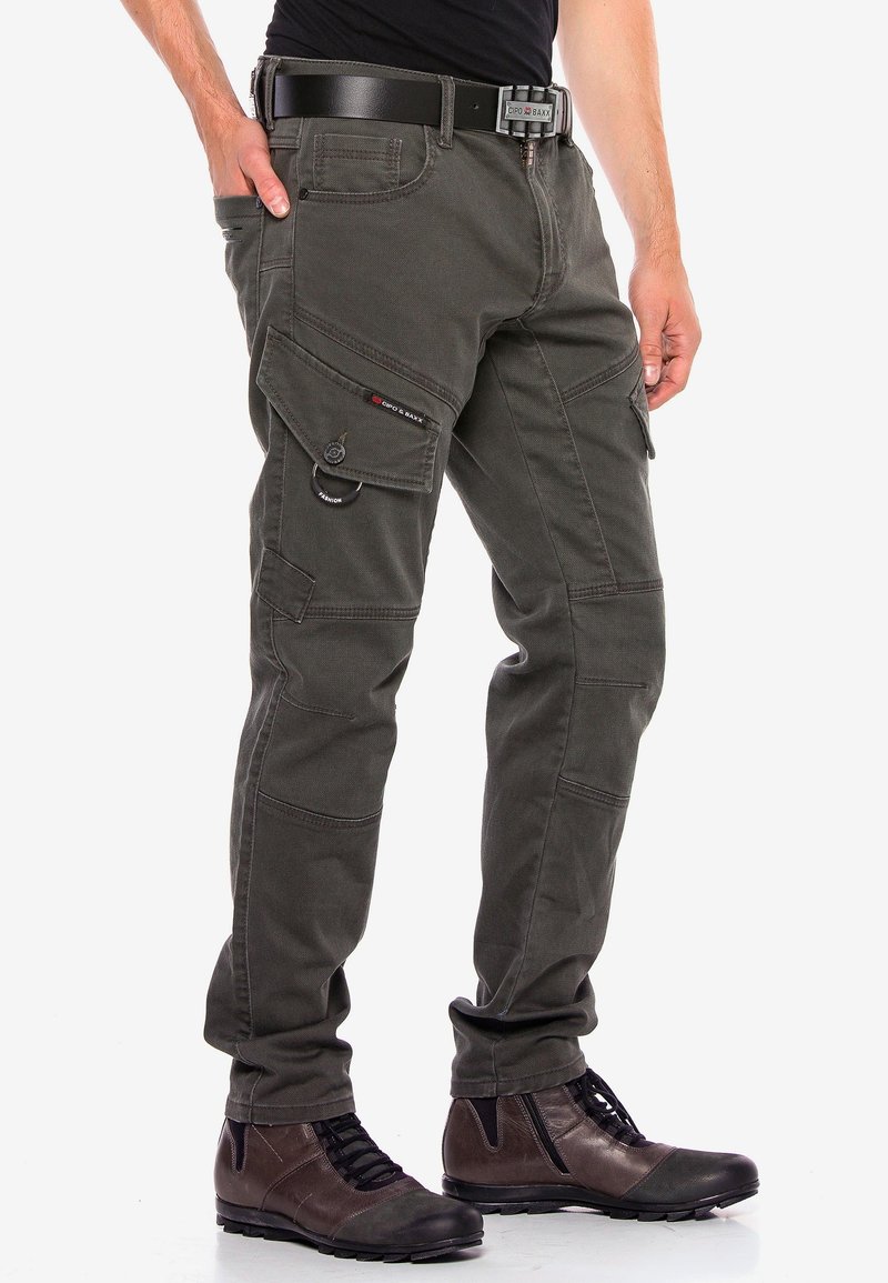 Cargo broek in donkergroene katoen, met meerdere zakken, stiksels en een riemlus. Gepaard met bruin veterschoenen.