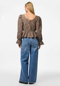 Top peplum marrone texturizzato con maniche a sbuffo, abbinato a jeans in denim blu a gamba larga a vita alta. La vista posteriore mostra un collo a barca.
