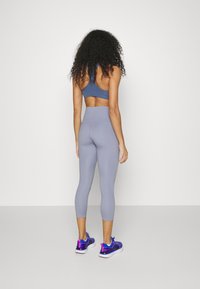 Szare legginsy z wysokim stanem w połączeniu z niebieskim stanikiem sportowym, prezentujące gładką teksturę i dopasowany krój. Niebieskie sneakersy dopełniają outfit.