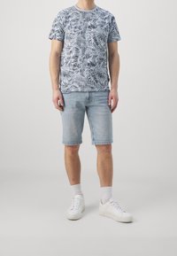 Men's outfit featuring a blue patterned short-sleeve t-shirt, light denim shorts, and white sneakers with matching socks.