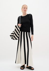 Melna garām piedurknēm virsjakas ar baltām maliņām, apvienota ar garu svārku ar vertikālām melnām un baltām svītrām. Iekļauts svītrains somiņas un melnas sandales.